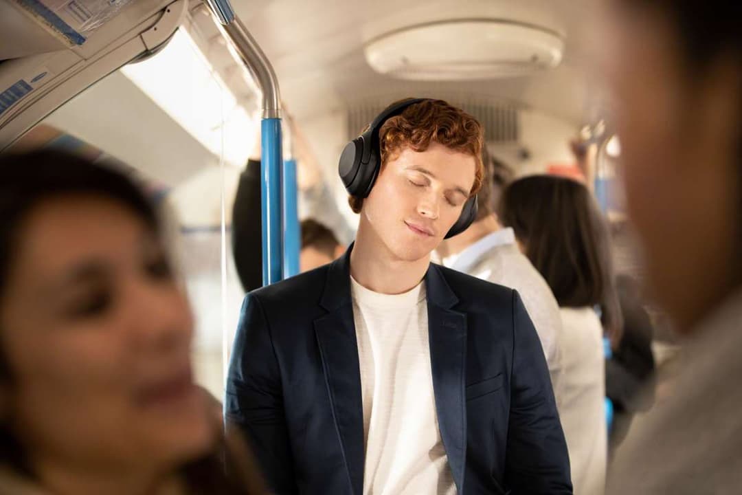 Jeune homme portant un casque Sony WH-1000XM4 noir dans les transports en commun, écoutant de la musique