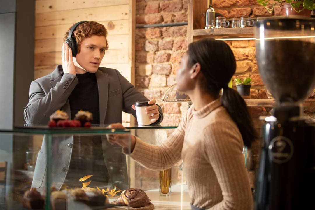 Sony WH-1000XM4 blanc porté par un homme en conversation avec une femme dans un intérieur moderne