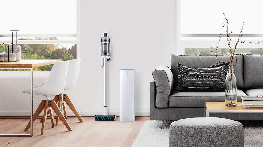 Samsung Clean Station blanche à côté du Samsung Jet gris dans un salon moderne avec canapé gris et mobilier contemporain