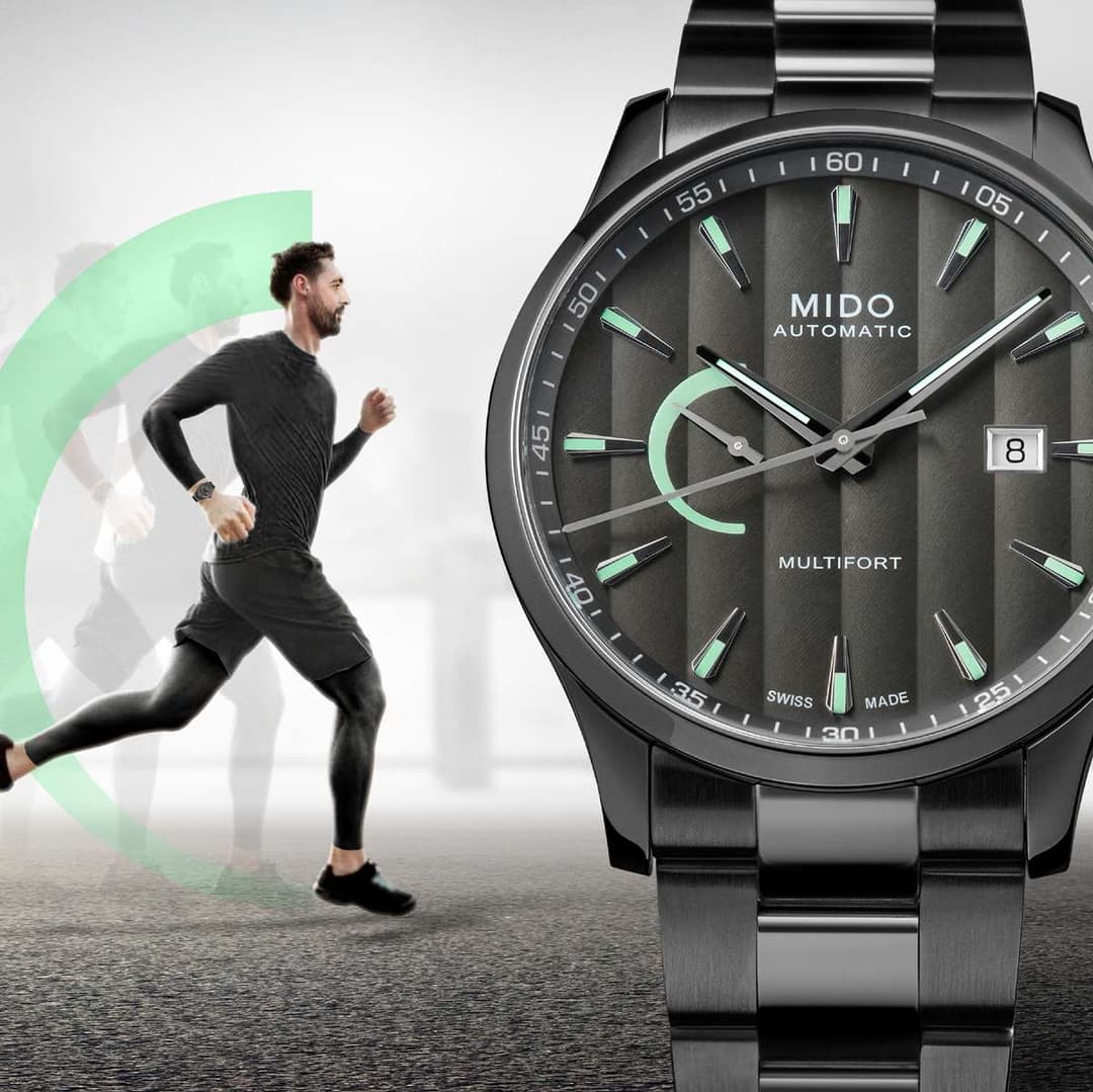Montre Mido Multifort Power Reserve avec cadran gris foncé, index verts et affichage de réserve de marche, à côté d'un coureur en tenue noire