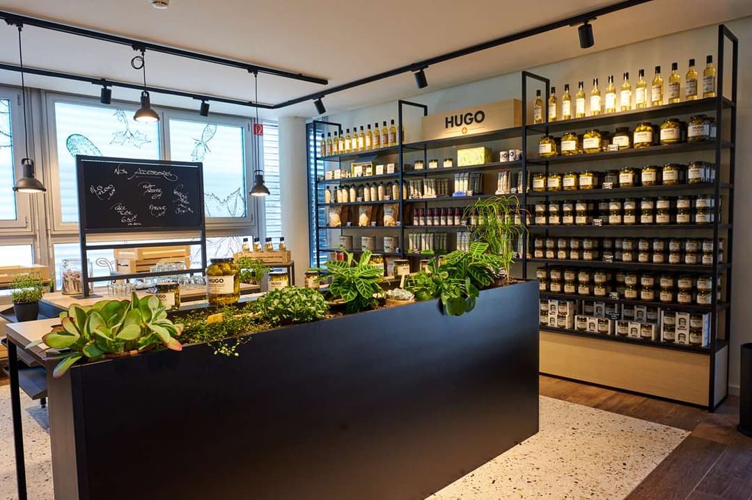 Intérieur du Hugo Shop à Aigle avec comptoir noir, étagères remplies de bocaux de produits Reitzel, plantes vertes et tableau noir