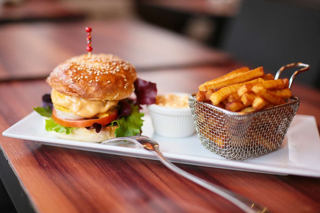 Burger garni de fromage et tomate avec frites dorées servies dans un panier métallique