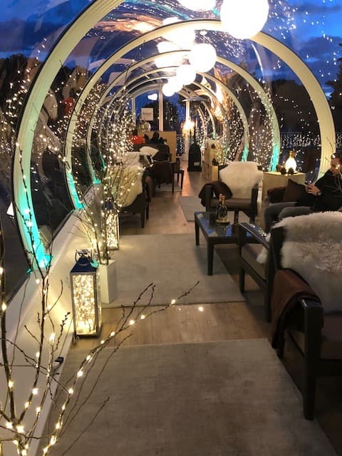 Intérieur de la bulle Ruinart Evasion du Beau-Rivage Palace, décorée de guirlandes lumineuses blanches et bleues, avec fauteuils et tables de café