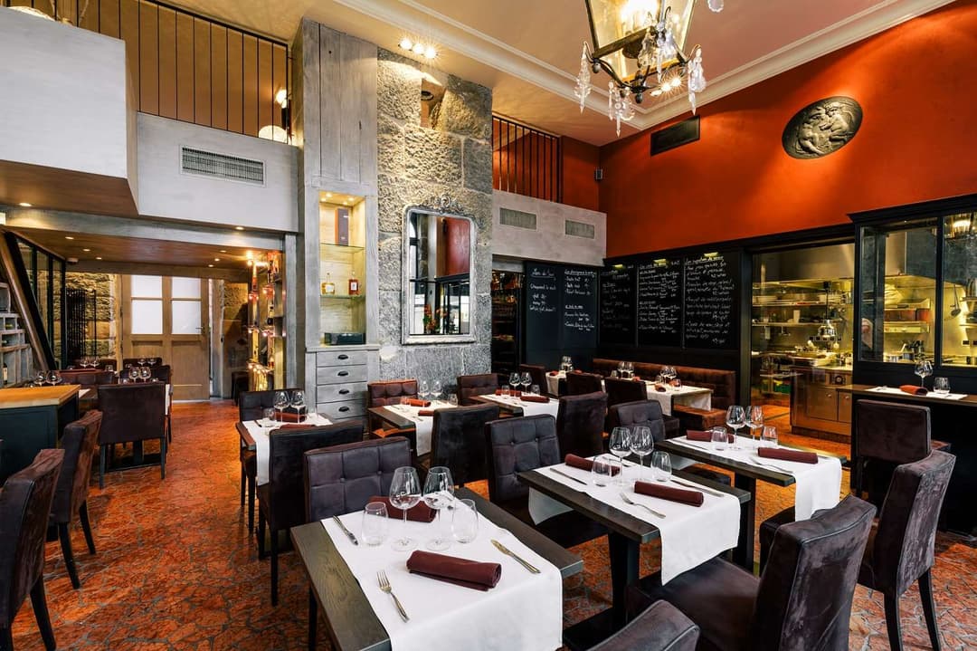 Salle de restaurant élégante aux murs orange et noir, tables dressées avec nappes blanches et serviettes bordeaux, chaises en velours foncé
