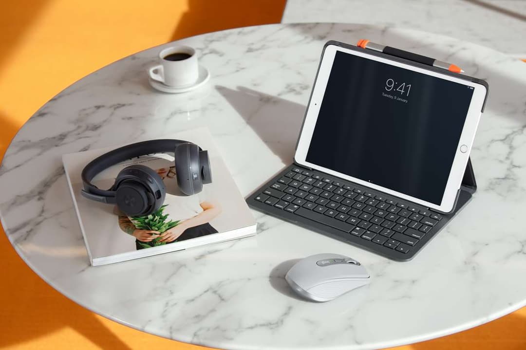 Souris Logitech MX Anywhere 3 grise sur un bureau en marbre blanc, avec une tablette, un clavier et des écouteurs