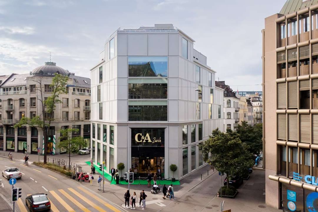 Façade du nouveau magasin C&A Zurich, bâtiment moderne en fibre-ciment blanc avec grandes fenêtres et logo doré, entouré de bâtiments historiques