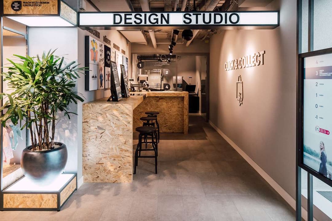 Intérieur du magasin C&A de Zurich avec espace Design Studio, comptoir en liège, plantes vertes et signalétique murale épurée