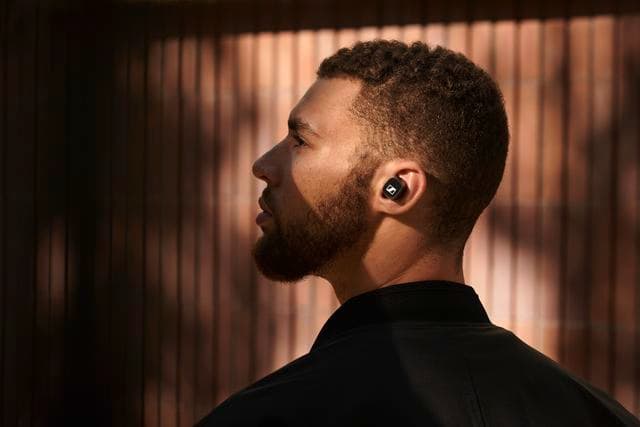 Homme portant un écouteur sans fil Sennheiser à l'oreille, de profil sur fond de rideaux dorés