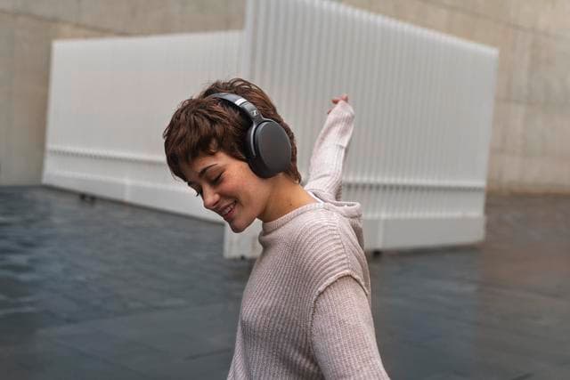 Personne portant un casque circum-auriculaire Sennheiser noir et blanc, souriante, vêtue d'un pull beige clair