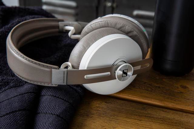 Casque Sennheiser HD 450BT blanc et gris avec arceau beige, posé sur tissu bleu marine et bois