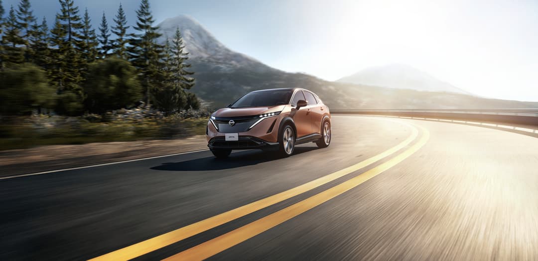 Nissan Ariya couleur bronze roulant sur une route sinueuse entourée de sapins et de montagne