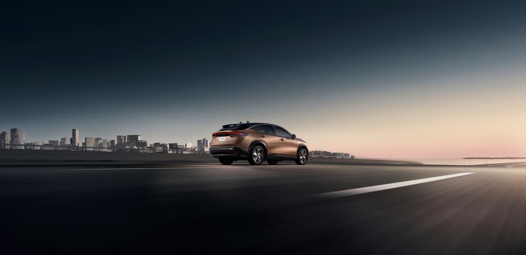 Nissan Ariya coupé crossover électrique de couleur bronze sur une route avec skyline urbaine en arrière-plan