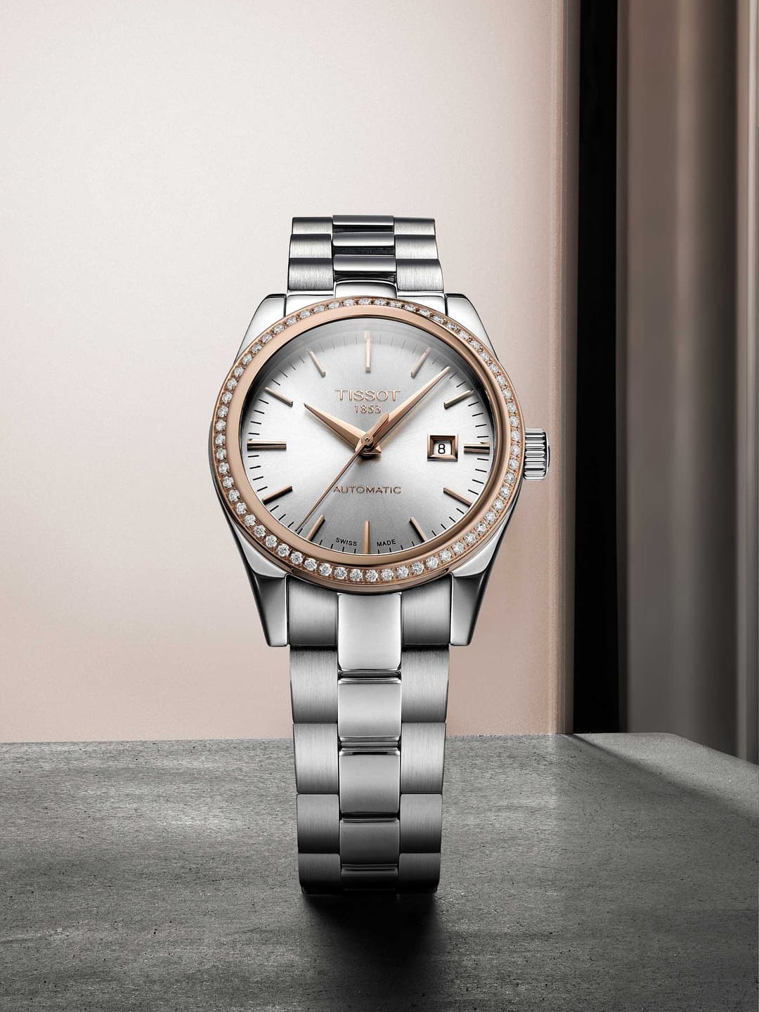 Montre Tissot T-My Lady, boîtier or rose et acier, cadran blanc, lunette sertie de diamants, bracelet acier, sur fond rose et gris