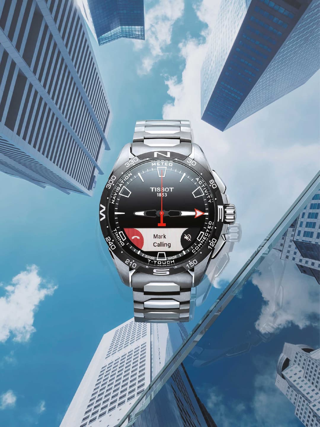 Montre Tissot acier avec cadran noir et affichage numérique Mark Calling, photographiée de face entourée de gratte-ciel modernes sous un ciel bleu
