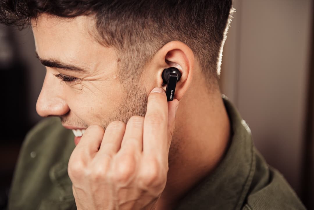 Homme portant un écouteur sans fil noir à l'oreille, en profil, souriant légèrement