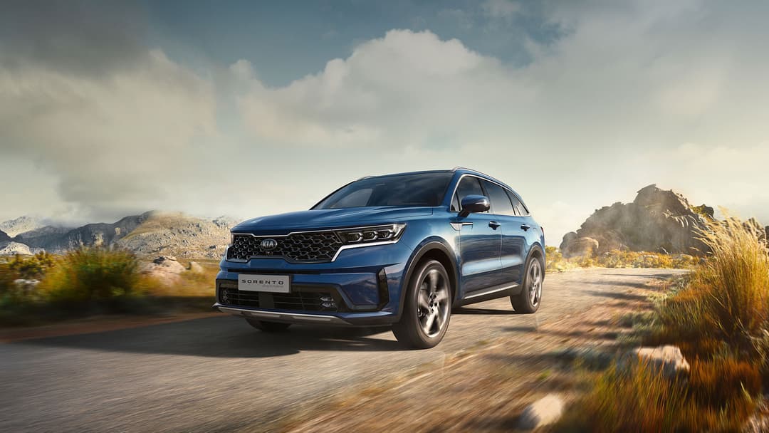 Kia Sorento bleu en mouvement sur une route désertique, montagnes rocheuses en arrière-plan
