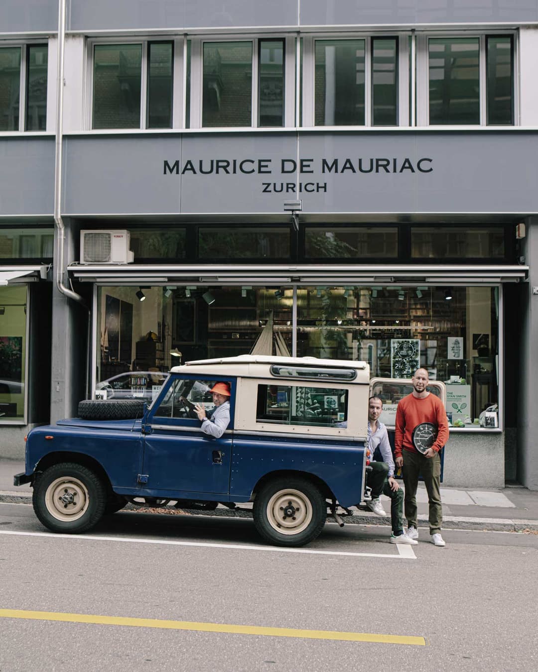 Trois personnes posent devant la boutique Maurice de Mauriac à Zurich, l'un dans un Land Rover Defender bleu et blanc