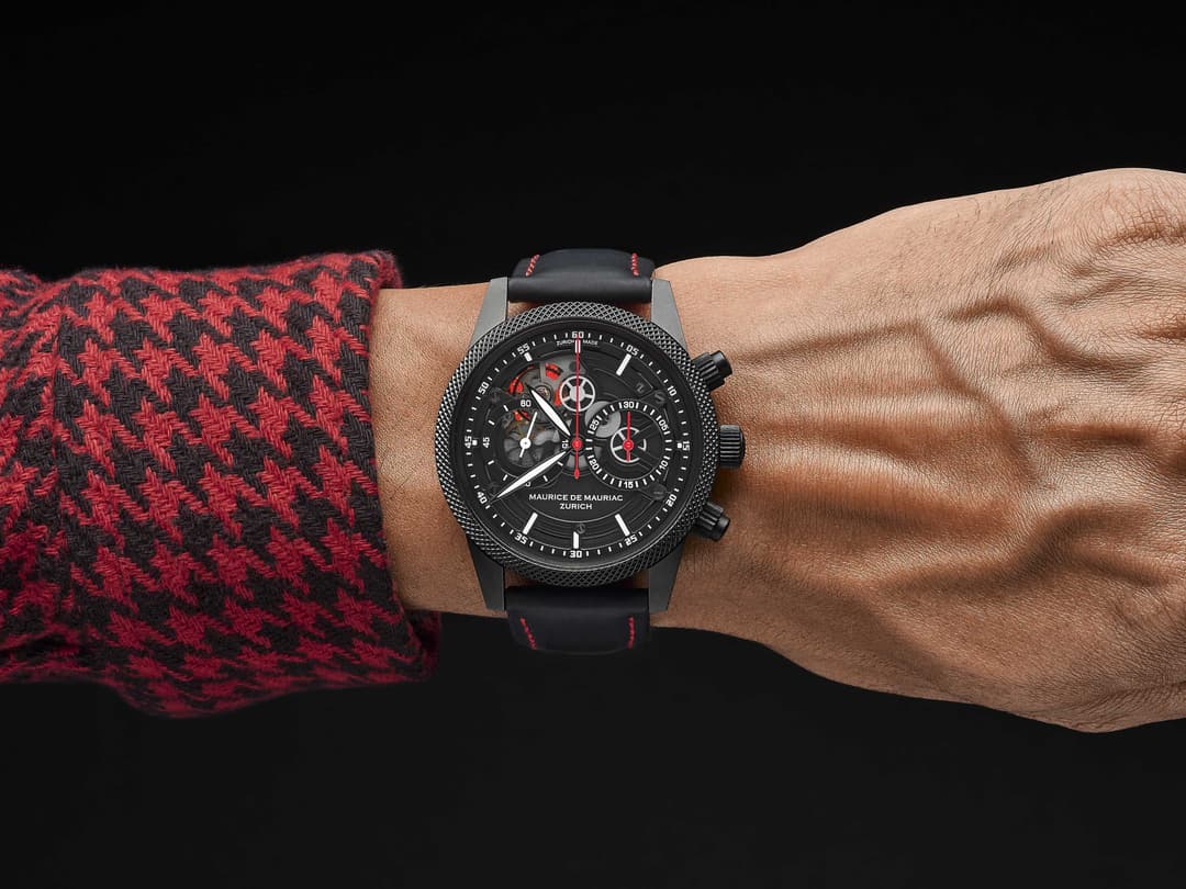 Montre Grand Cœur Maurice de Mauriac au cadran noir avec détails rouges, portée au poignet avec un pull rouge et noir