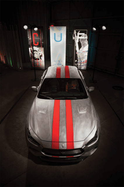Maserati MC20 grise avec bandes rouges, vue de face, présentée dans un espace d'exposition avec panneaux illuminés