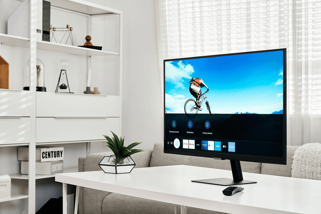 Samsung Smart Monitor affichant une vidéo de cycliste et l'interface de streaming avec Netflix, HBO et YouTube sur un bureau blanc