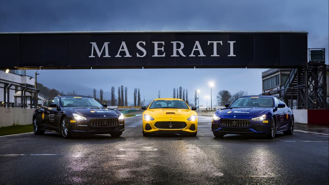 Trois voitures Maserati alignées sur une piste, noire, jaune et bleue, sous un portique noir avec le logo Maserati