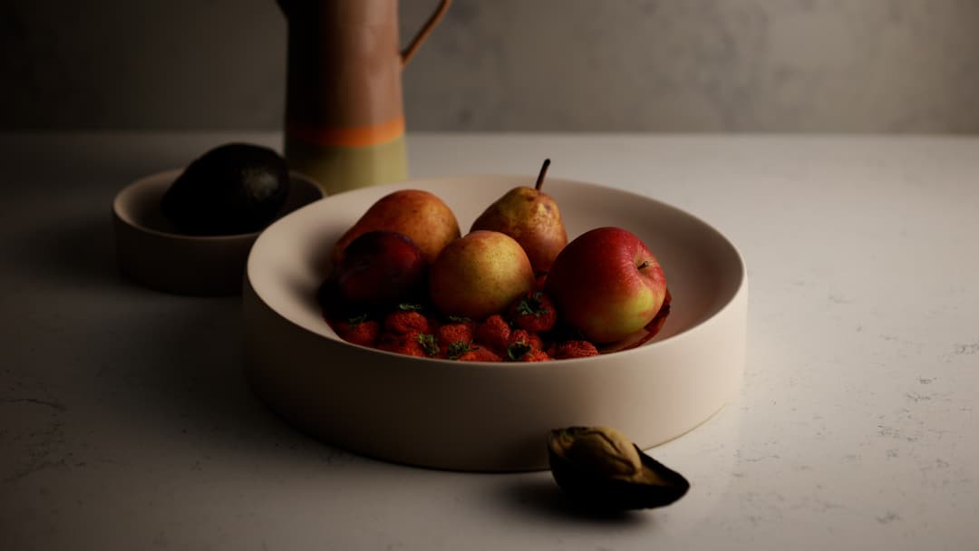 Bol blanc contenant des poires, des pommes rouges et des fraises, avec un petit bol de fruits noirs en arrière-plan