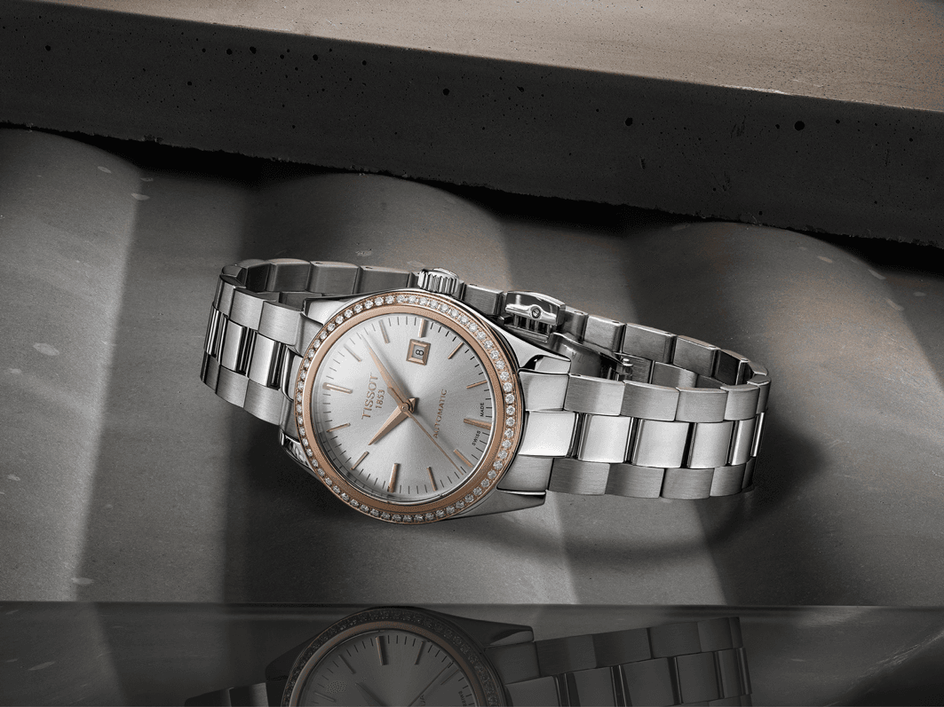 Montre Tissot en acier avec boîtier serti de diamants, cadran blanc et bracelet interchangeable, sur fond gris