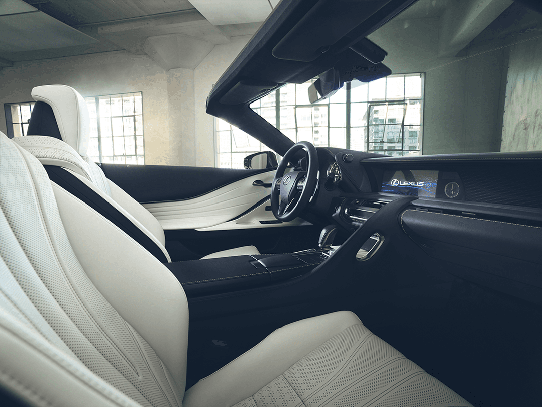 Intérieur du Lexus LC 500 Cabriolet avec sièges blanc et noir, toit ouvert et volant, vue depuis le siège passager
