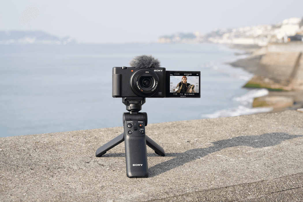 Sony ZV-1 avec microphone et stabilisateur sur trépied, écran articulé affichant un présentateur, en bord de mer