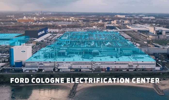Aérienne de l'usine Ford de Cologne avec son logo bleu et blanc, bâtiments de production turquoise, fleuve en premier plan et ville allemande en arrière-plan