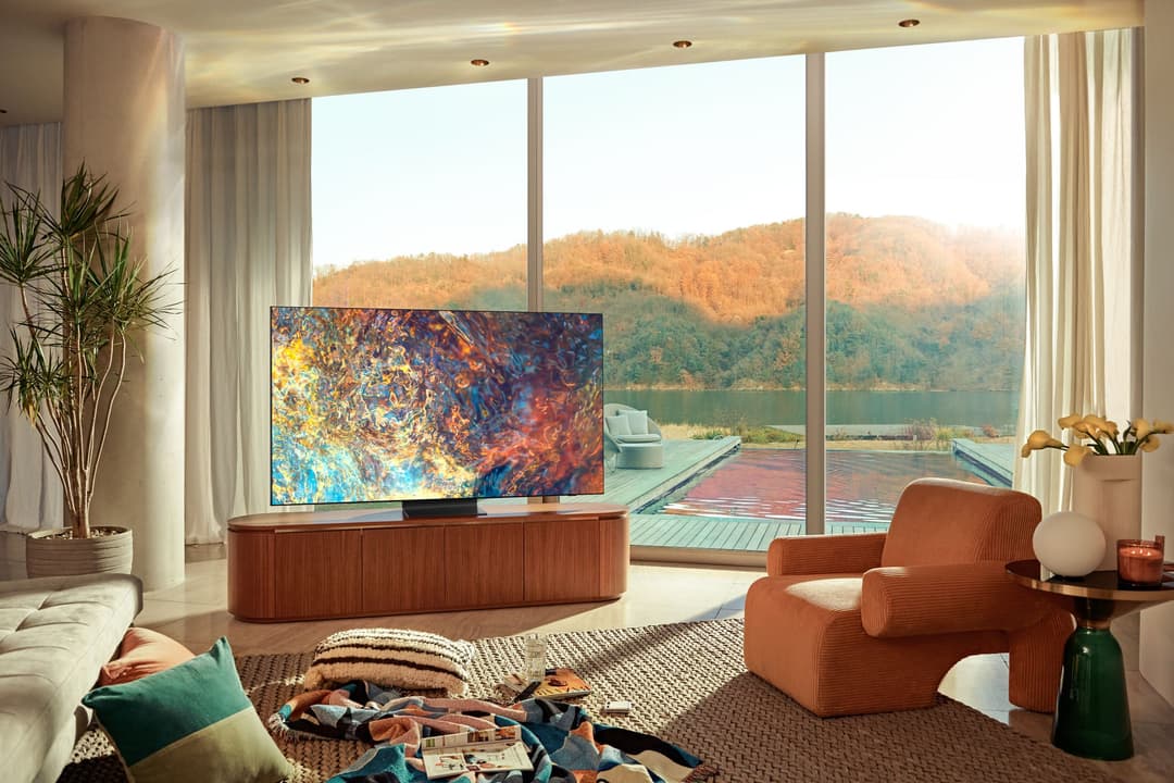 Samsung Neo QLED affichant une abstraction colorée dans un salon moderne avec vue panoramique sur un lac et des montagnes boisées