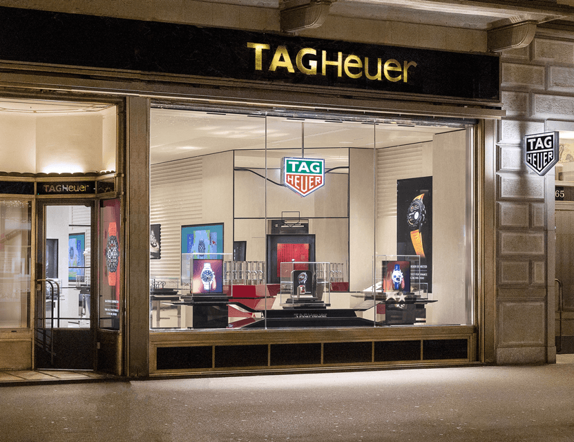 Devanture de la boutique flagship TAG Heuer à Zurich avec enseigne dorée, vitrines éclairées présentant des montres et le logo TAG Heuer illuminé