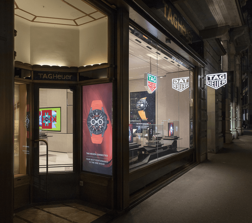 Boutique flagship TAG Heuer à Zürich, façade vitrée la nuit avec montres exposées et logos de la marque