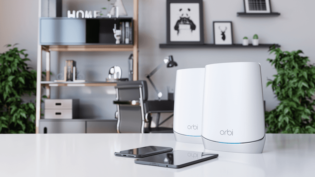 Deux routeurs Netgear Orbi blancs et un smartphone posés sur un bureau blanc, intérieur moderne en arrière-plan