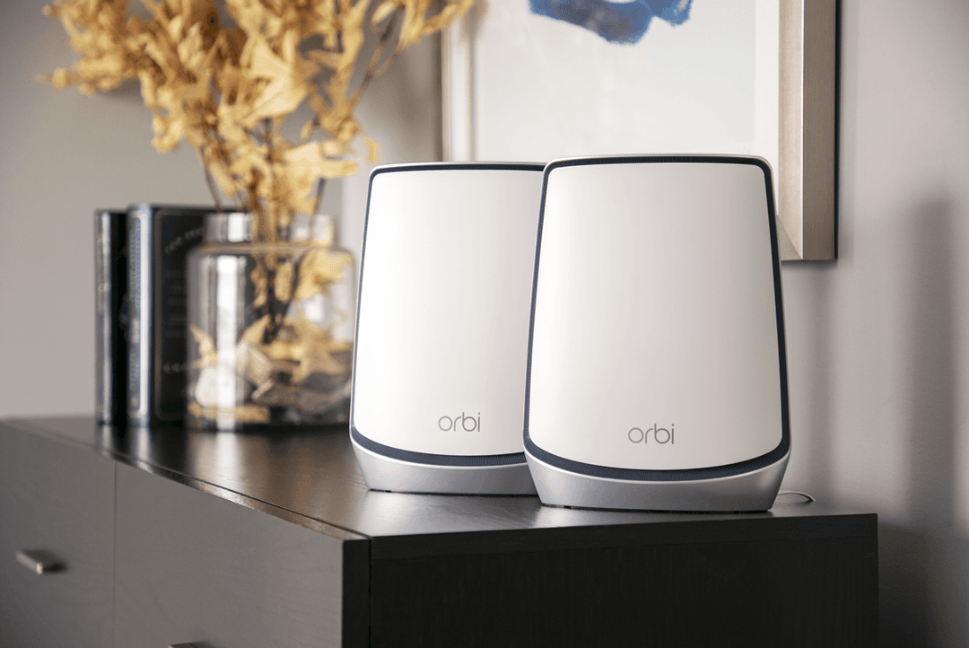 Deux boîtiers Netgear Orbi blancs avec bordure noire posés sur un meuble noir dans un intérieur moderne
