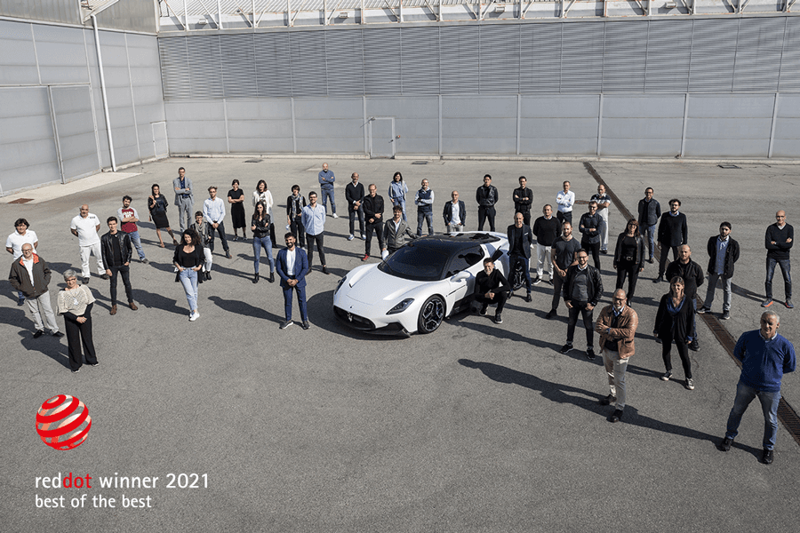 Maserati MC20 blanche, portes papillon ouvertes, entourée de l'équipe de designers et d'ingénieurs sur un parking couvert