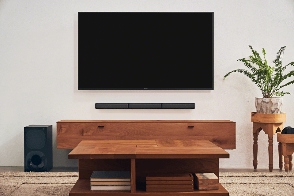 Système audio Sony HT-S40R dans un salon : barre sonore noire murale, caisson de basses, téléviseur et mobilier en bois