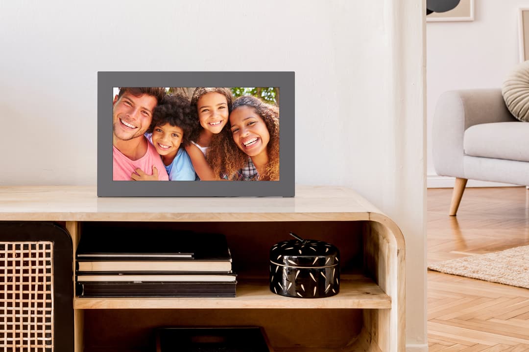 Cadre Photo Connecté Meural de Netgear 15,6 pouces affichant une photo de famille souriante, posé sur un meuble en bois dans un salon