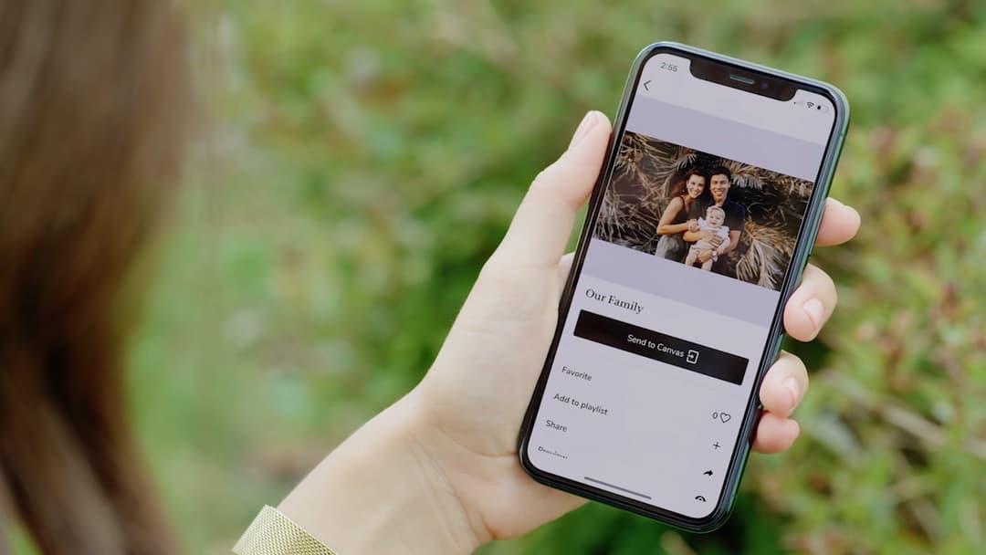 Main tenant un smartphone affichant l'application Meural avec une photo de famille et l'option d'envoi vers le cadre connecté