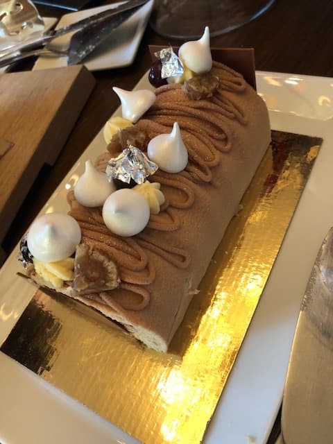 Bûche au chocolat et aux marrons garnie de boules blanches et de carrés argentés, sur un présentoir doré