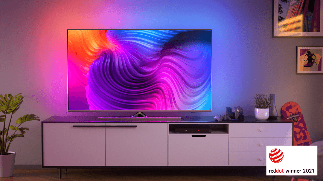 Téléviseur Philips affichant des motifs ondulés colorés rose, bleu et orange, posé sur un meuble avec logo Red Dot Winner 2021