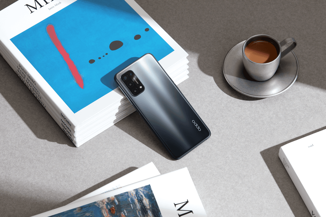 Smartphone OPPO noir avec ses quatre capteurs photo, posé entre un magazine et une tasse de café sur fond gris