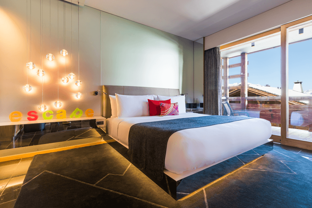 Chambre du W Verbier avec lit blanc et coussins rouges, luminaires suspendus, décoration contemporaine et balcon vue montagne