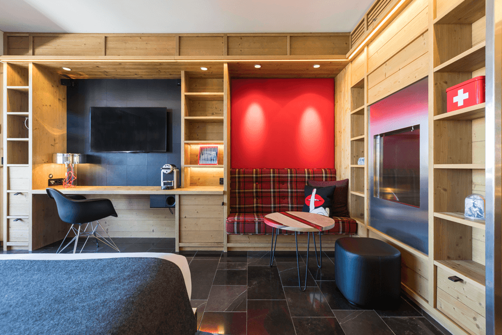 Salon du W Verbier avec banquette à motif montagnard rouge, table basse en chêne et résine rose flua, coussins brodés et mur rouge vif
