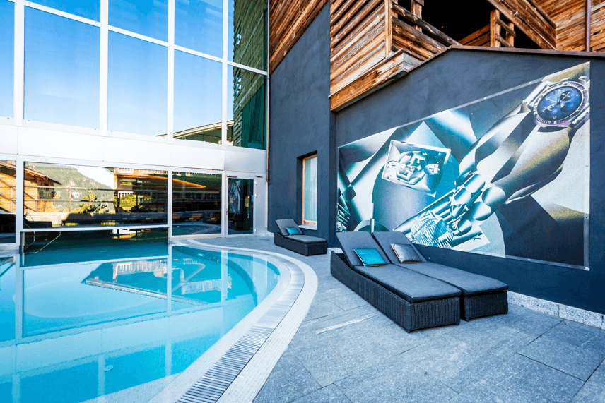 Espace bien-être du W Verbier avec piscine intérieure turquoise, bains à remous, et transats noirs face à une fresque murale
