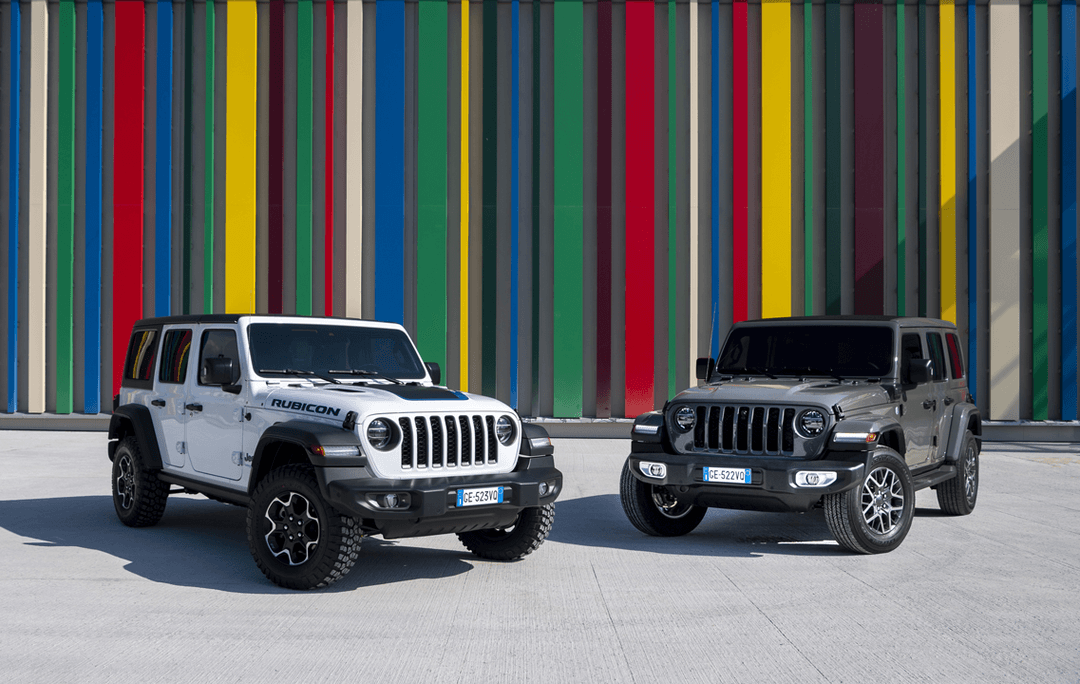 Deux Jeep Wrangler Unlimited 4xe côte à côte, l'une blanche et l'autre gris foncé, devant un mur coloré aux bandes multicolores