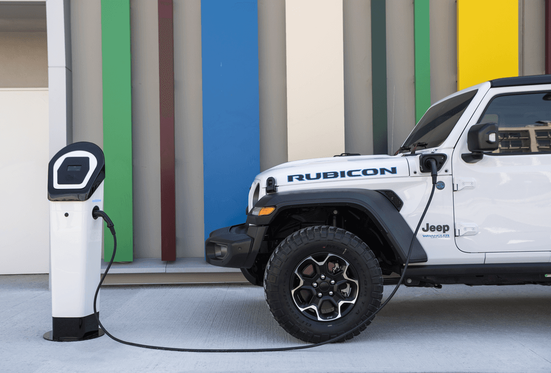 Jeep Wrangler Unlimited 4xe blanche branchée à une borne de recharge électrique devant un mur coloré
