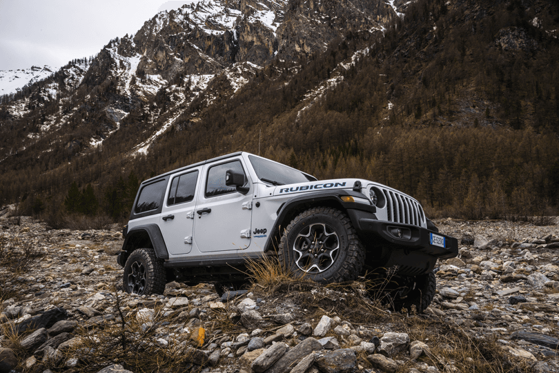 Jeep Wrangler Unlimited 4xe blanche et noire garée sur terrain rocheux en montagne enneigée