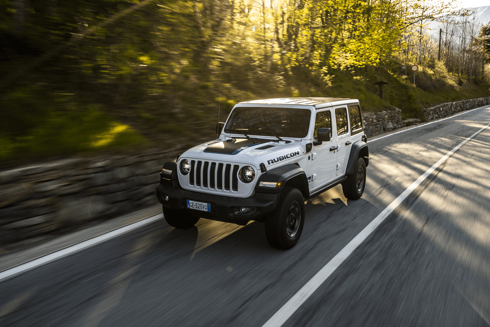 Jeep Wrangler Unlimited 4xe blanc et noir roulant sur une route de montagne bordée de forêt