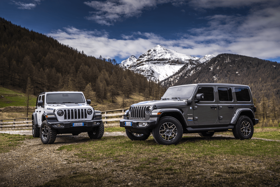 Deux Jeep Wrangler Unlimited 4xe, une blanche et une grise, garées face à un paysage montagneux enneigé avec forêts de sapins